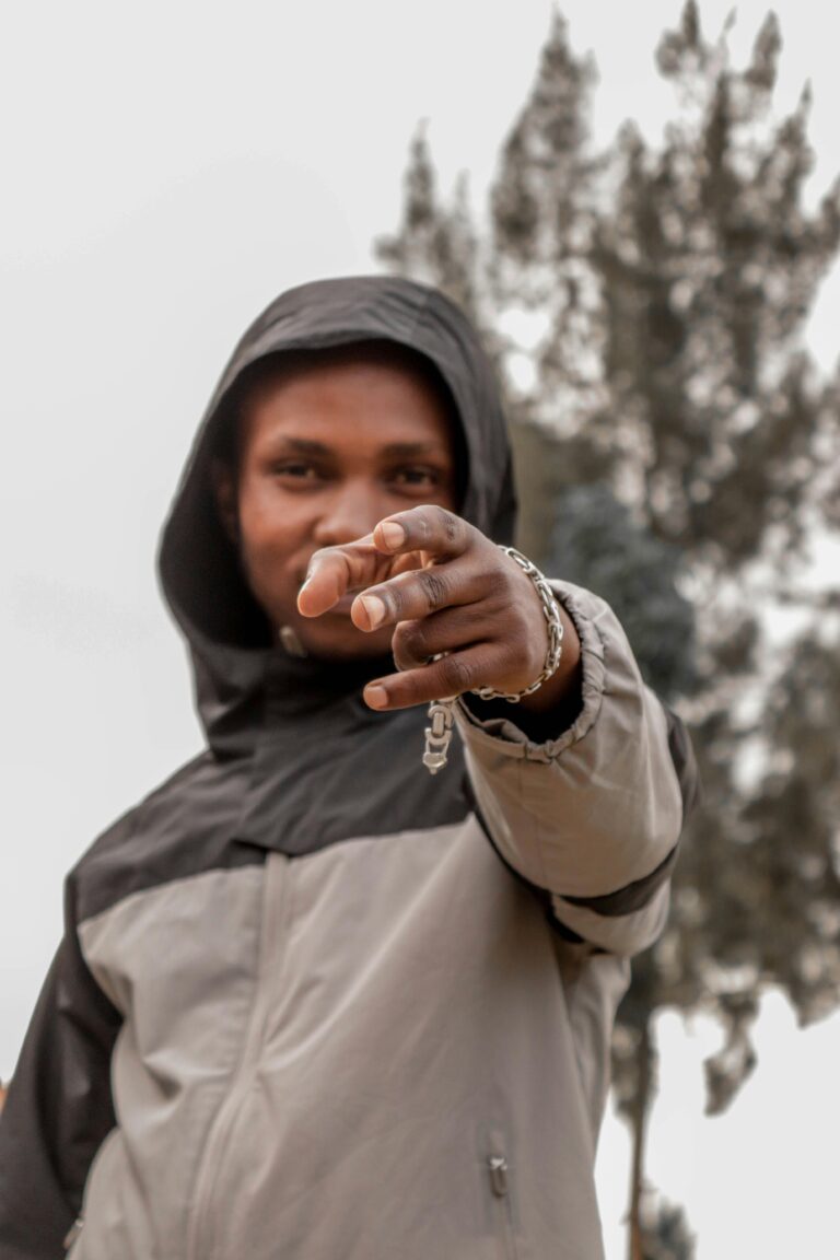A man in a hoodie confidently pointing at the camera in an outdoor setting.
